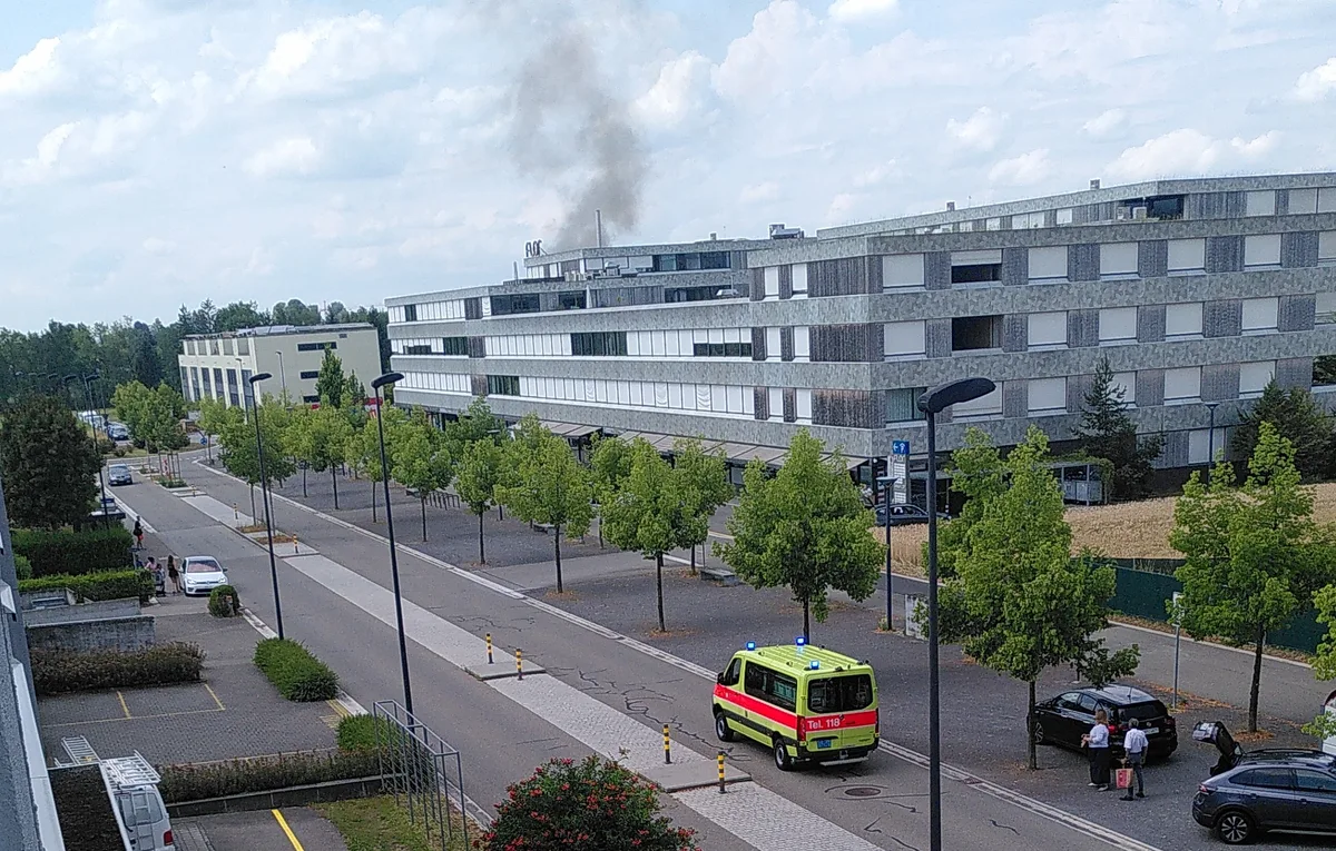Rauchwolken steigen über Uster West auf. Man sieht eine Strasse mit einem Feuerwehrauto.